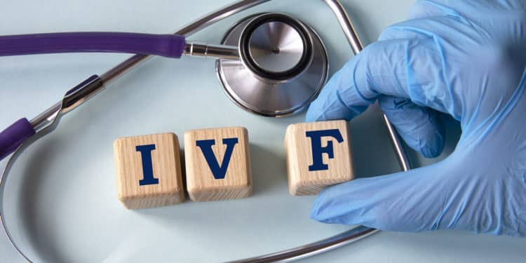 A hand in a medical glove puts cubes with the abbreviation IVF on the background of a stethoscope. Medication infertility