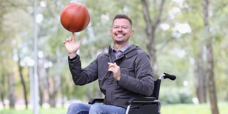 Portrait of happy smiling disabled man twirling basketball ball. Guy sitting in wheelchair in urban park. Disability and healthcare concept